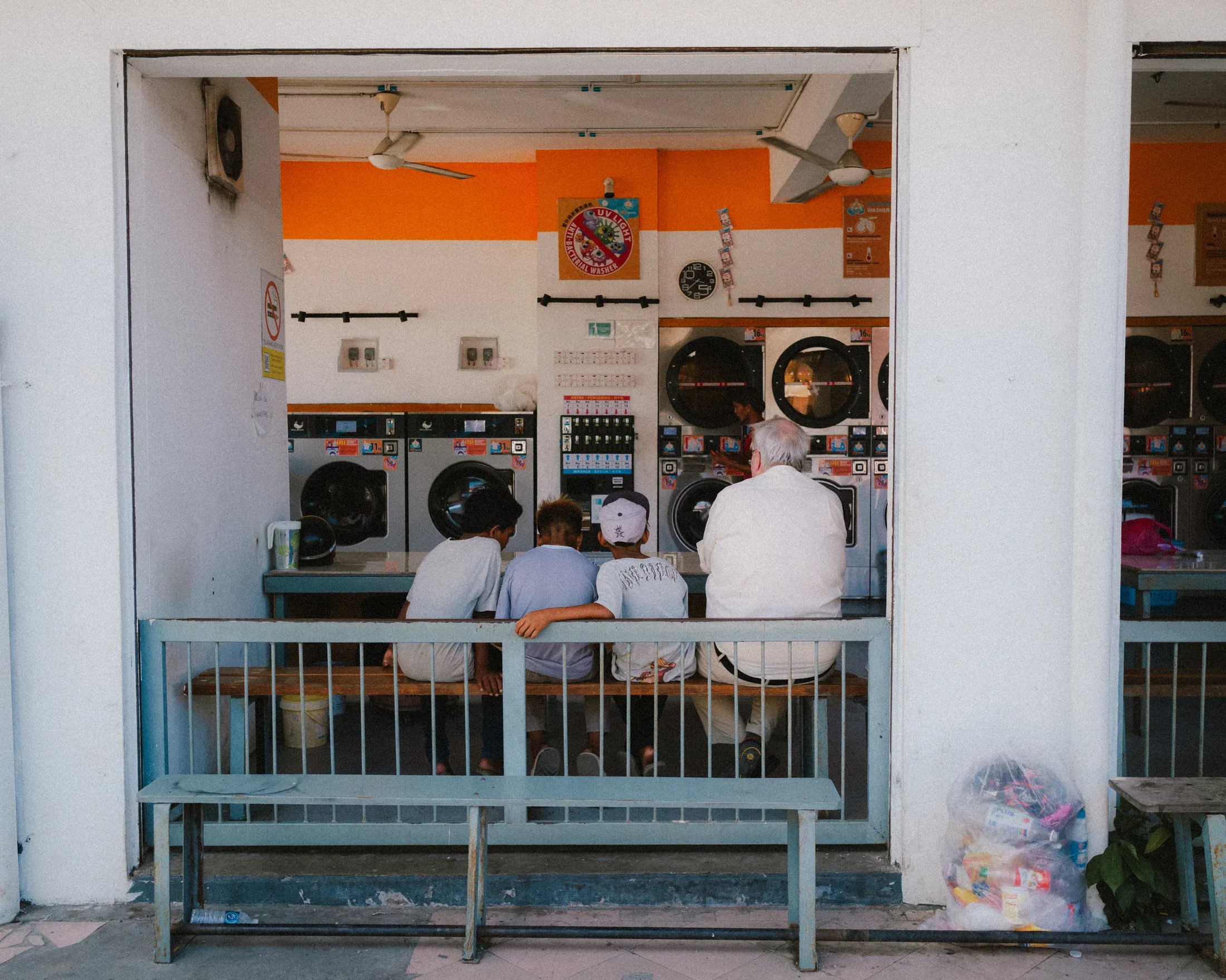 Diners seen from behind at the open window of a small orange and white restaurant.