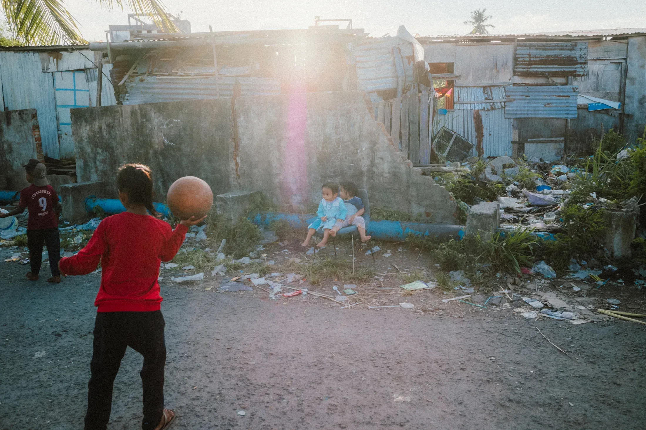 Children playing beside improvised homes as low sunlight flares across the frame.
