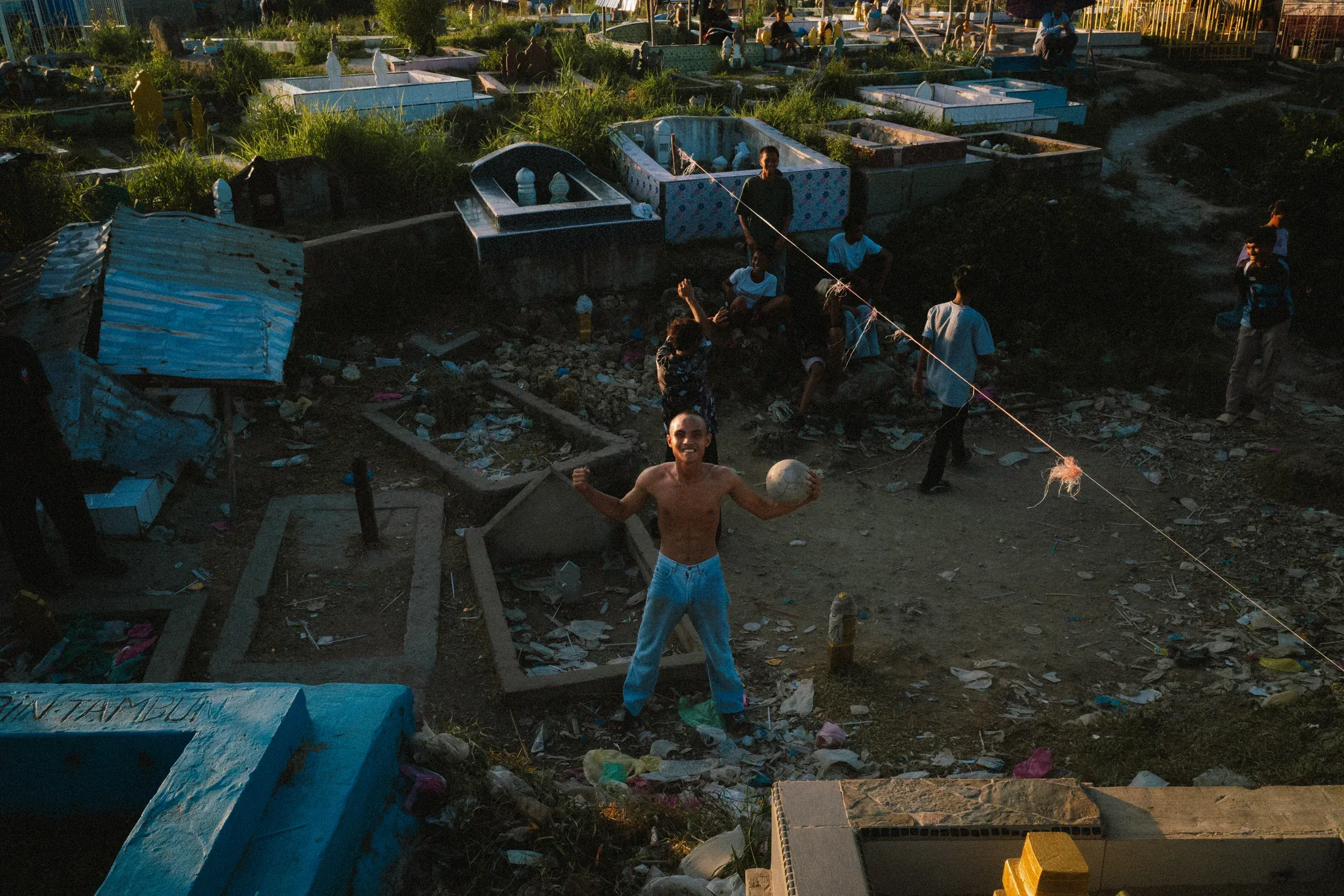 Shirtless man looking up while children move among low homes and rough ground.