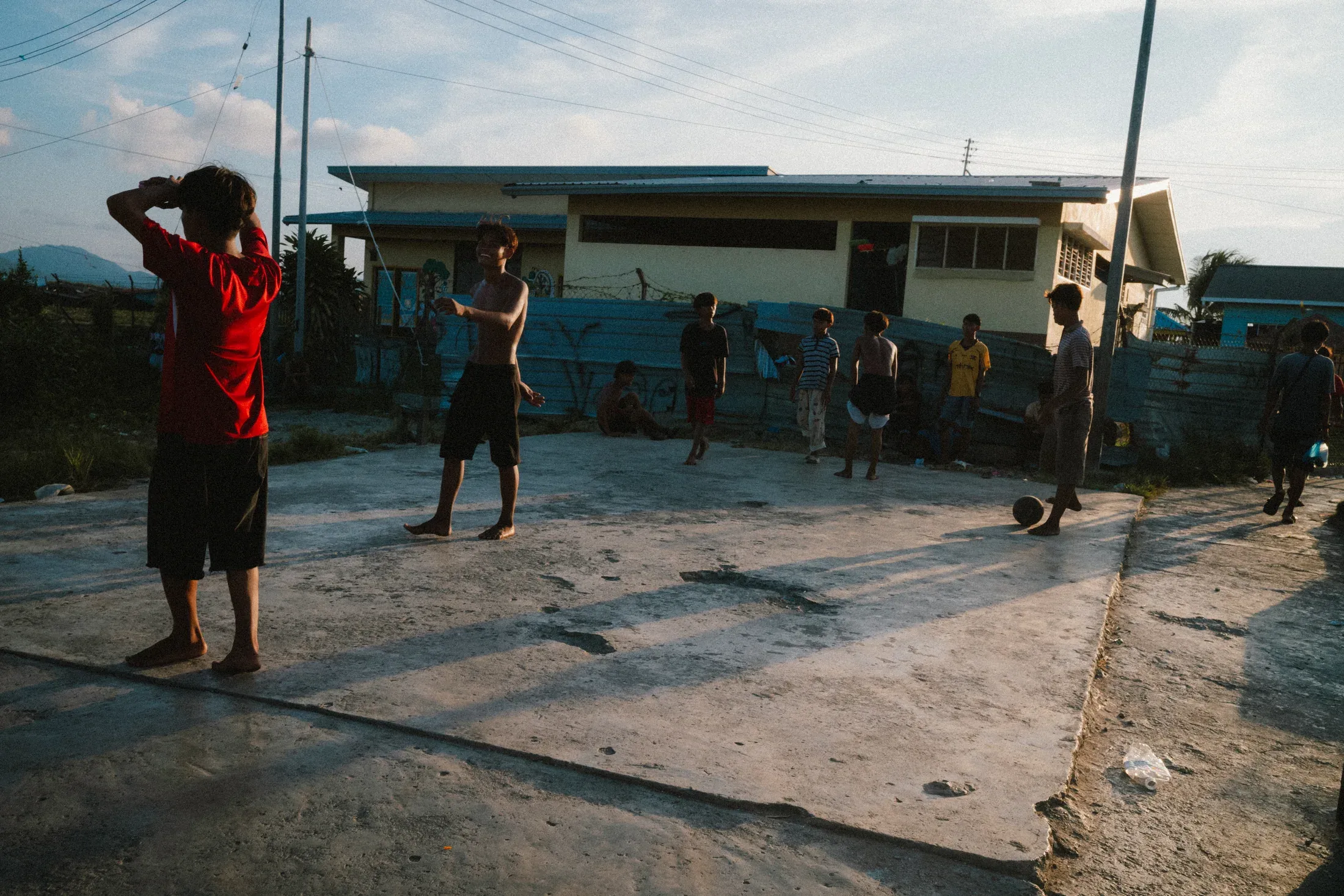 Children gathered on a concrete court between modest coastal houses.
