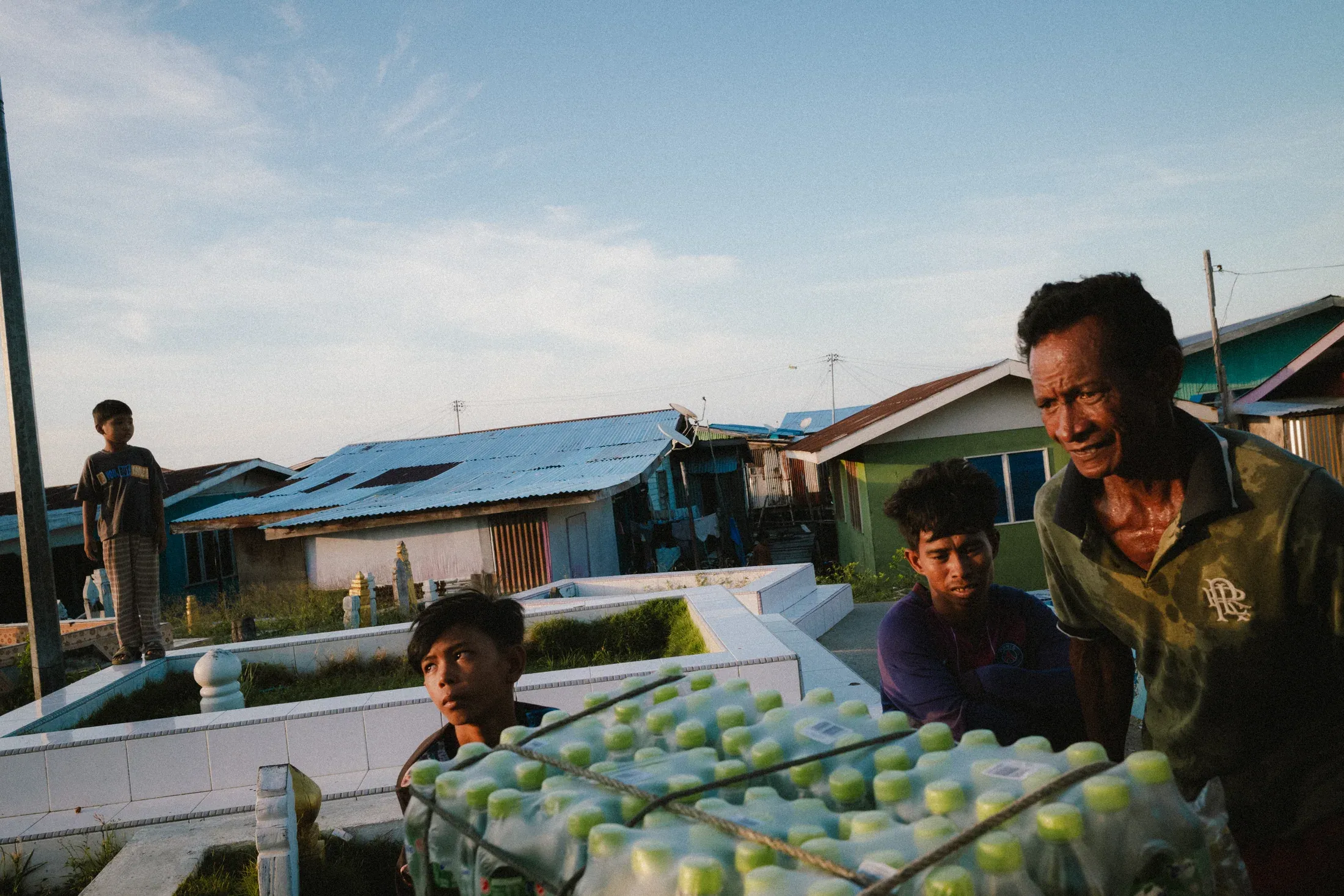 Two boys and a laughing vendor behind a table covered with pale green fruit.