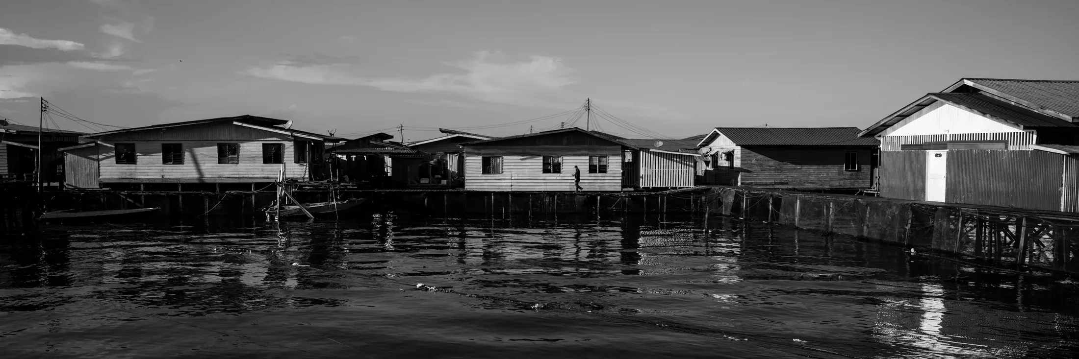 Black and white panorama of wooden houses standing over calm coastal water.